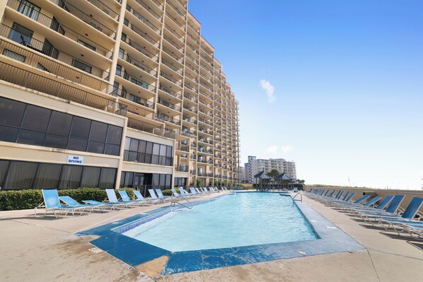A swimming pool with lounge chairs, a 'No Diving' sign, and a high-rise building in the background.