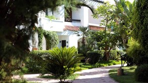 Un chemin menant à un bâtiment doté d’un toit en tuiles, entouré d’une végétation luxuriante et d’un jardin bien entretenu.