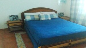 Une chambre à coucher avec un lit en bois, une literie bleue, deux tables de chevet et une petite table de nuit avec une lampe.