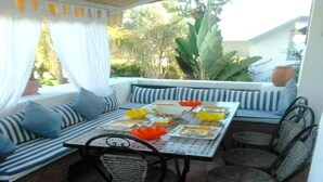 Un coin repas avec une table dressée pour quatre personnes, entourée de chaises en osier et de coussins à rayures.