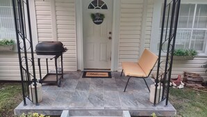 En veranda med en grill, en stol och en välkomstmatta.