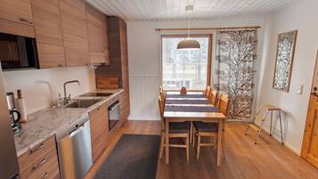 Una cocina moderna con armarios de madera, lavavajillas de acero inoxidable y una zona de comedor con mesa y sillas de madera.