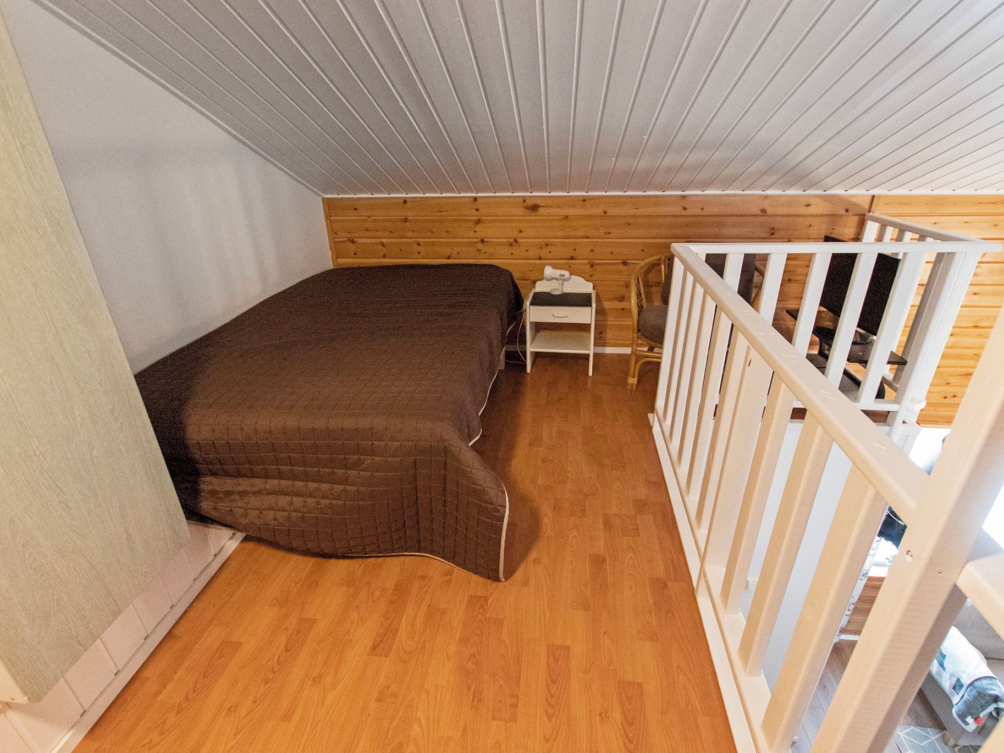 Une petite chambre avec un lit simple, un plancher en bois et une rambarde blanche.