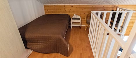 A small, single-bed room with a wooden floor and a white railing.