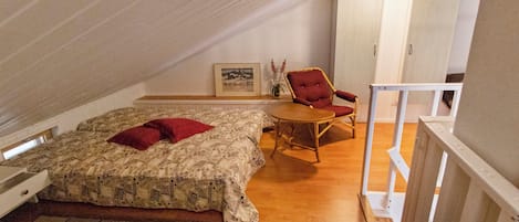 Une chambre à coucher avec un lit, une chaise, un tableau au mur et un plancher en bois.
