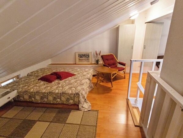 A bedroom with a bed, a chair, a picture on the wall, and a wooden floor.