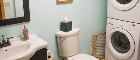 A bathroom with a sink, toilet, and stacked washing machines.
