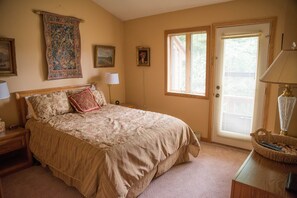A bedroom with a large bed, a nightstand, a lamp, a door with blinds, and a tapestry on the wall.