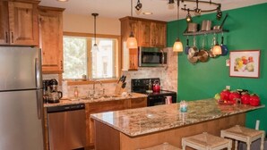 A kitchen with wooden cabinets, a granite island with bar stools, a stainless steel refrigerator, and a green accent wall. - Cozy, Beautifully Furnished Condo 10  Minutes to Ski Resorts (Davis)
