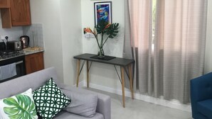 A modern living room with a grey sofa, a small black table, and a kitchen area with wooden cabinets and a stove.