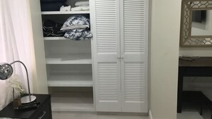A bedroom with a white wardrobe, a bedside table with a lamp, and a mirror on the wall.