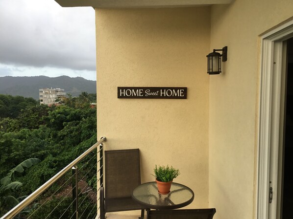 A balcony with a chair, a small table, and a potted plant. A sign on the wall reads "HOME Sweet HOME". - Home sweet home  for best accommodation business and pleasure one u will enjoy. (Castries)