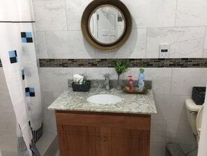 A bathroom with a marble sink, a wooden vanity, a round mirror, and toiletries on the counter. - Home sweet home  for best accommodation business and pleasure one u will enjoy. (Castries)