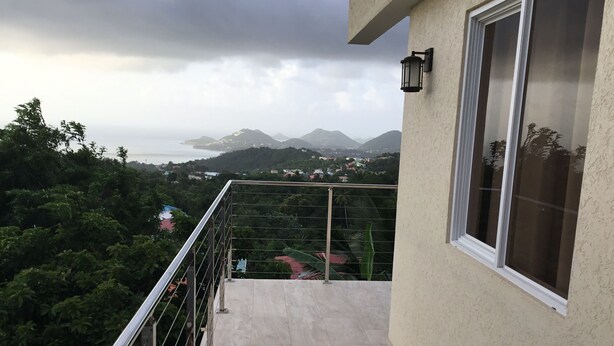 A balcony with a view of a coastal landscape, including mountains and a body of water.
