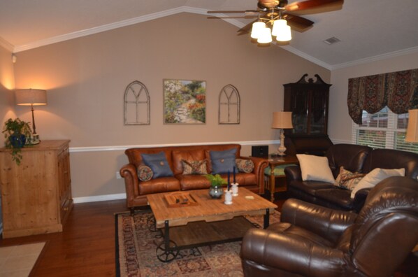 A living room with a brown leather sofa, a wooden coffee table, and a ceiling fan. - Magnolia Gardens NEW (Grovetown)