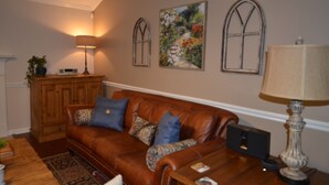 A living room with a brown leather sofa, a wooden cabinet, a lamp, and two framed pictures on the wall. - Magnolia Gardens NEW (Grovetown)
