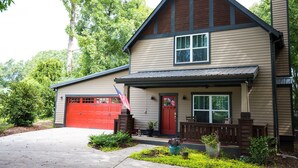 A two-story house with a red garage door, a front porch with a bench, and a small garden area. - Game day 3/2. 5 in charming Watkinsville downtown! (Watkinsville)