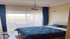 Een slaapkamer met een bed, een hanglamp, een raam met gordijnen en uitzicht op het omliggende landschap.