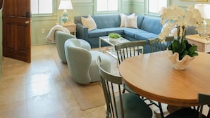 Een eethoek met een ronde houten tafel, stoelen, een blauwe bank en een hanglamp.