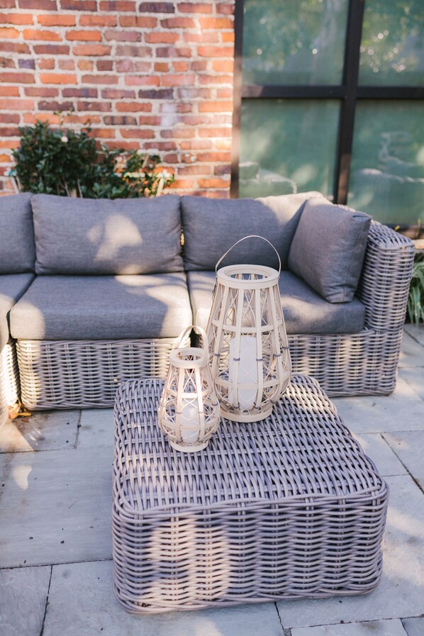 Relax in a serene outdoor space with a comfortable sofa and matching ottoman, surrounded by lush greenery and a brick wall.