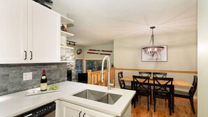 A modern kitchen with white cabinets, a built-in dishwasher, and a dining area with a wooden table and chairs. - Ski to the door!True SI/SO Luxury 2BrTH-Private HT (Whistler)