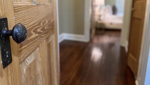 Une porte en bois avec un bouton noir, qui donne sur un couloir au plancher de bois.