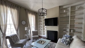 Un salon comprenant un canapé, des fauteuils, une table basse, un téléviseur et une bibliothèque.
