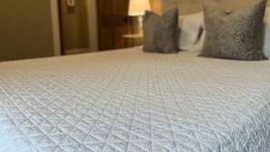 Un lit recouvert d’une couette blanche matelassée, avec deux oreillers et une lampe de chevet.
