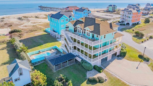 A coastal residential area with a prominent turquoise house featuring multiple balconies and a swimming pool. - Semi-Oceanfront Dog Friendly Home w/ Pool, Hot Tub, EV Charger, Game Room, More! (Rodanthe)