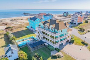 A coastal residential area with a prominent turquoise house featuring multiple balconies and a swimming pool. - Semi-Oceanfront Dog Friendly Home w/ Pool, Hot Tub, EV Charger, Game Room, More! (Rodanthe)