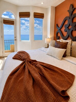 A hotel room with a bed, a view of the sea through windows, and a decorative wall piece. - Bella Sirena Oceanfront 3BR Penthouse – Steps from the Beach + Stunning Views! (Puerto Peñasco)
