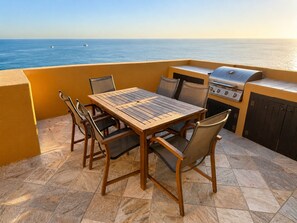 An outdoor patio with a table and chairs, a grill, and a view of the ocean. - Bella Sirena Oceanfront 3BR Penthouse – Steps from the Beach + Stunning Views! (Puerto Peñasco)