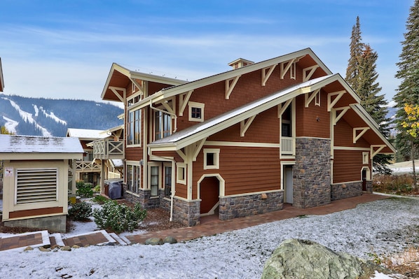 Un grand chalet à étages, doté d’imposantes fondations en pierre et d’une façade en bois, qui se dresse sur un paysage montagneux.