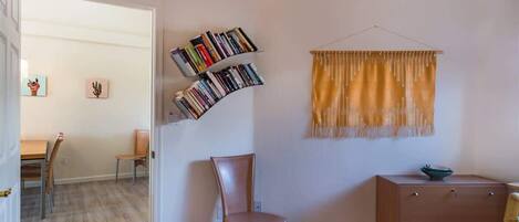 A room with a curved bookshelf, a single chair, a small cabinet, and a window with a yellow curtain.