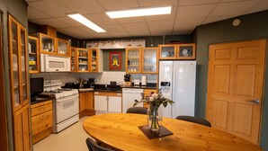 A kitchen with wooden cabinets, a white refrigerator, a stove, and a dining table with chairs. - Mindfulness Room - Good Karma Inn - Bed and Breakfast in Homer, Alaska (Homer)