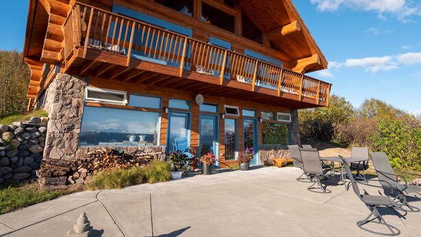A two-story log cabin with a balcony, stone foundation, and outdoor seating area. - Mindfulness Room - Good Karma Inn - Bed and Breakfast in Homer, Alaska (Homer)
