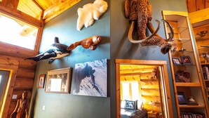 A cabin interior with wooden walls, a bed with a blue and white patterned bedspread, a wooden bookshelf, and various wall-mounted animal carvings. - Mindfulness Room - Good Karma Inn - Bed and Breakfast in Homer, Alaska (Homer)