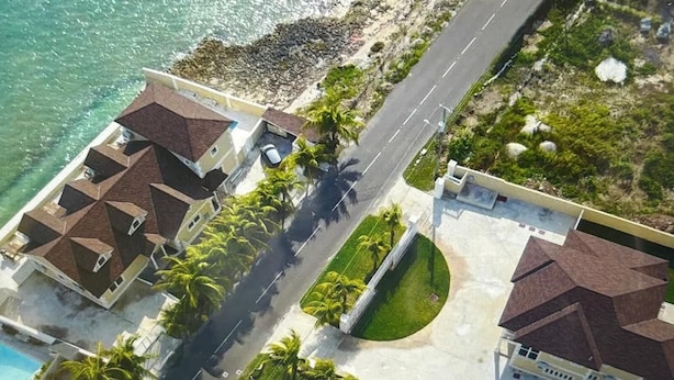 Ein Luftbild eines Küstengrundstücks mit mehreren Gebäuden, einer Straße und einem Strand.