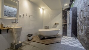 A modern bathroom with a freestanding bathtub, a large mirror, and a stone wall.