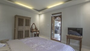 A bedroom with a large bed, a wooden wardrobe, a vanity with a mirror, and a television on a wooden stand.