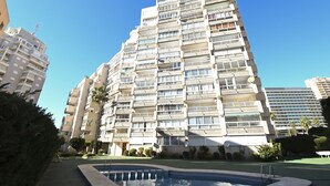 Un immeuble résidentiel de grande hauteur doté de nombreux balcons, d’une piscine et entouré de verdure.