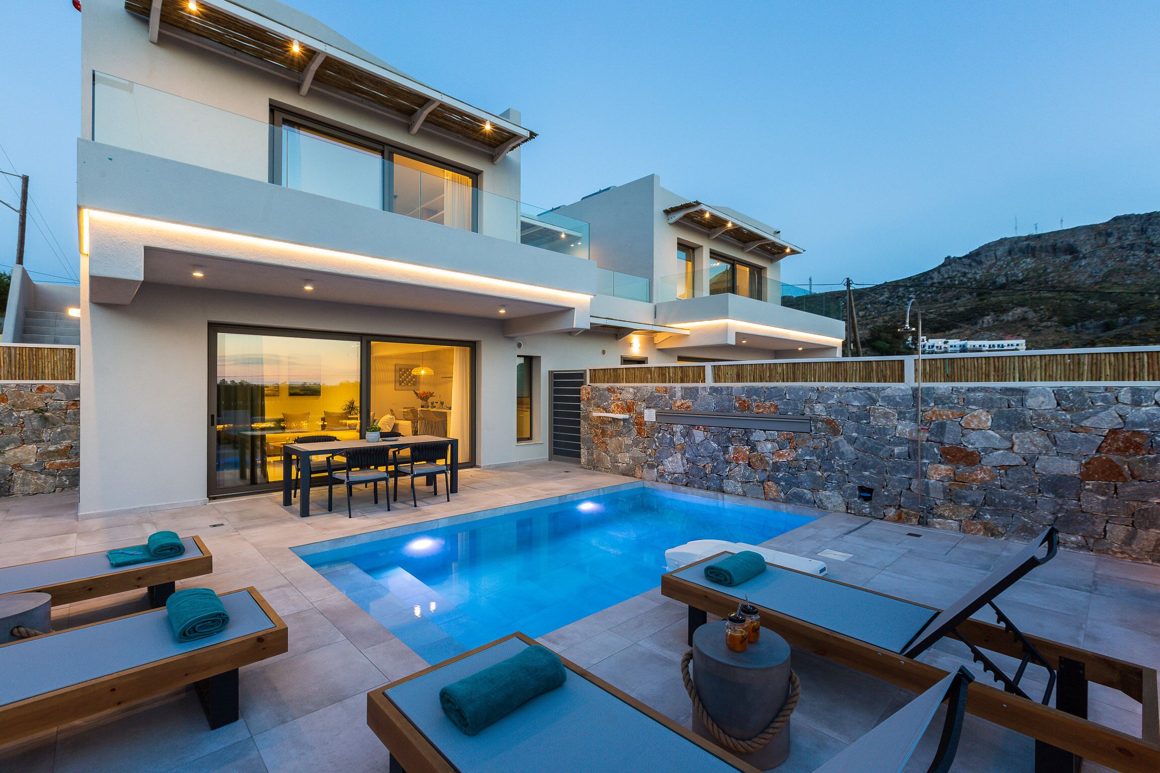 A modern two-story house with a swimming pool, outdoor seating, and a stone wall.