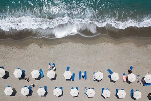 Luchtbeeld van een strand met rijen parasols en ligbedden, waarvan sommigen door mensen worden gebruikt.