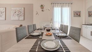 Comedor con una mesa dispuesta para cuatro, incluyendo platos, vasos y cubiertos. Hay dos sillas, un armario blanco y una ventana con cortinas.