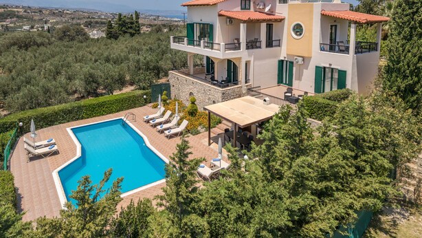 Una villa de varios pisos con piscina, mobiliario exterior y vistas del paisaje circundante.