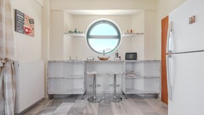 Una cocina compacta con un ventanal redondo, encimeras de mármol blanco y dos taburetes de bar.