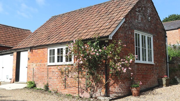 Ein Ziegelhaus mit einem Ziegeldach, einer weißen Garagentür und einem Rosenbusch im Vorgarten.