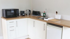Eine kompakte Küche mit weißen Schränken, einer Mikrowelle, einer Kaffeemaschine, einem Wasserkocher, einem Toaster und einem Geschirrspüler.