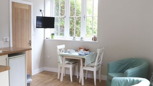 Eine kleine Küche mit Esstisch, Stühlen, einem kleinen Kühlschrank und einem Fernseher, der über dem Fenster befestigt ist.