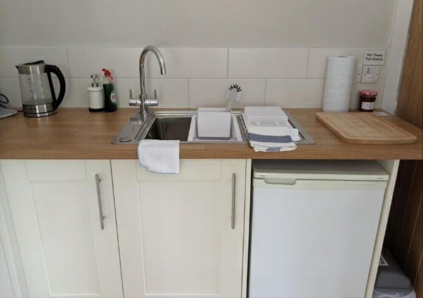 Een kleine keuken met een spoelbak, een koffiezetapparaat, een waterkoker en een afdruiprek.